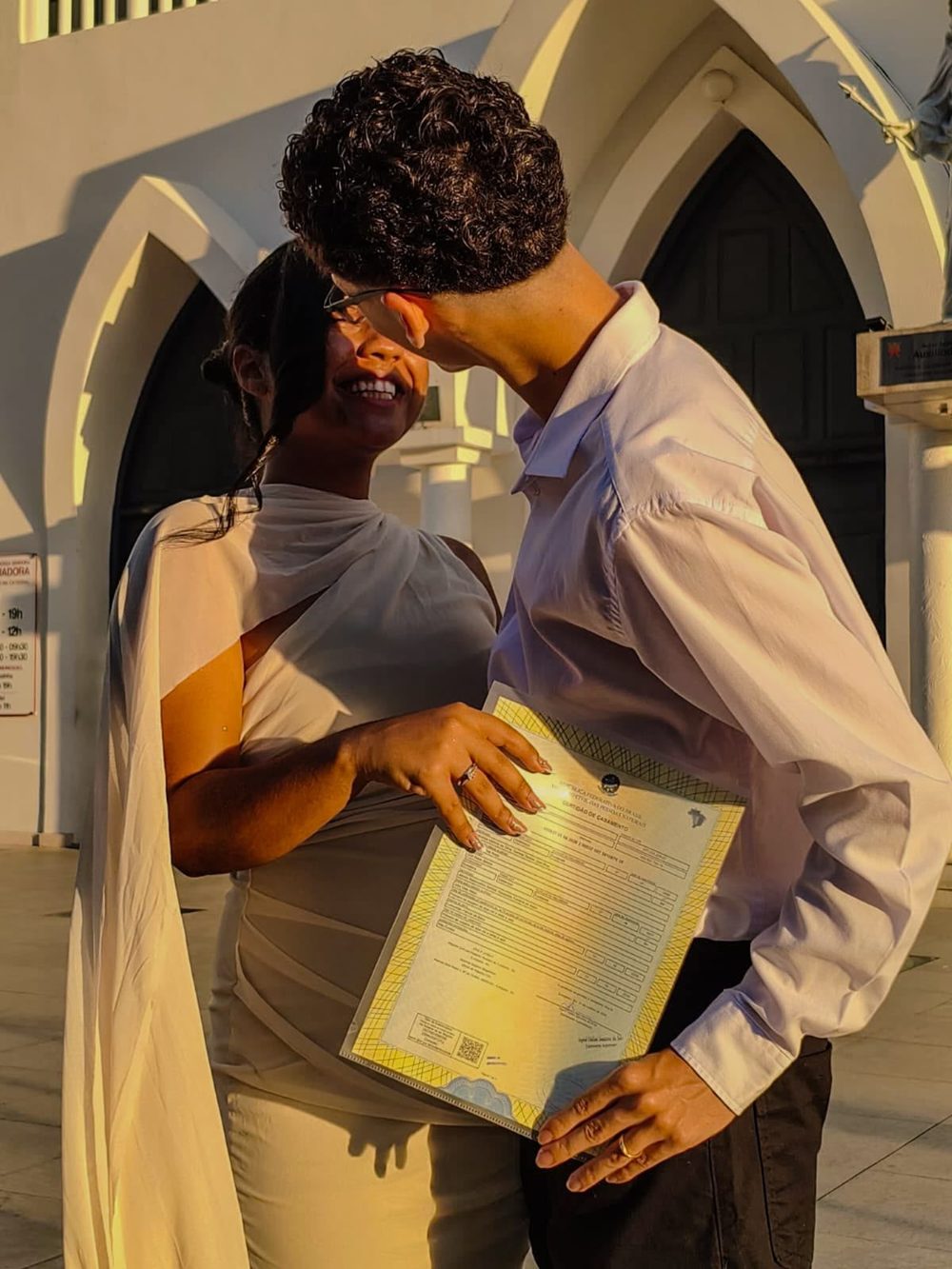 Emanuel e Julya segurando a certidão de casamento ao pôr do sol